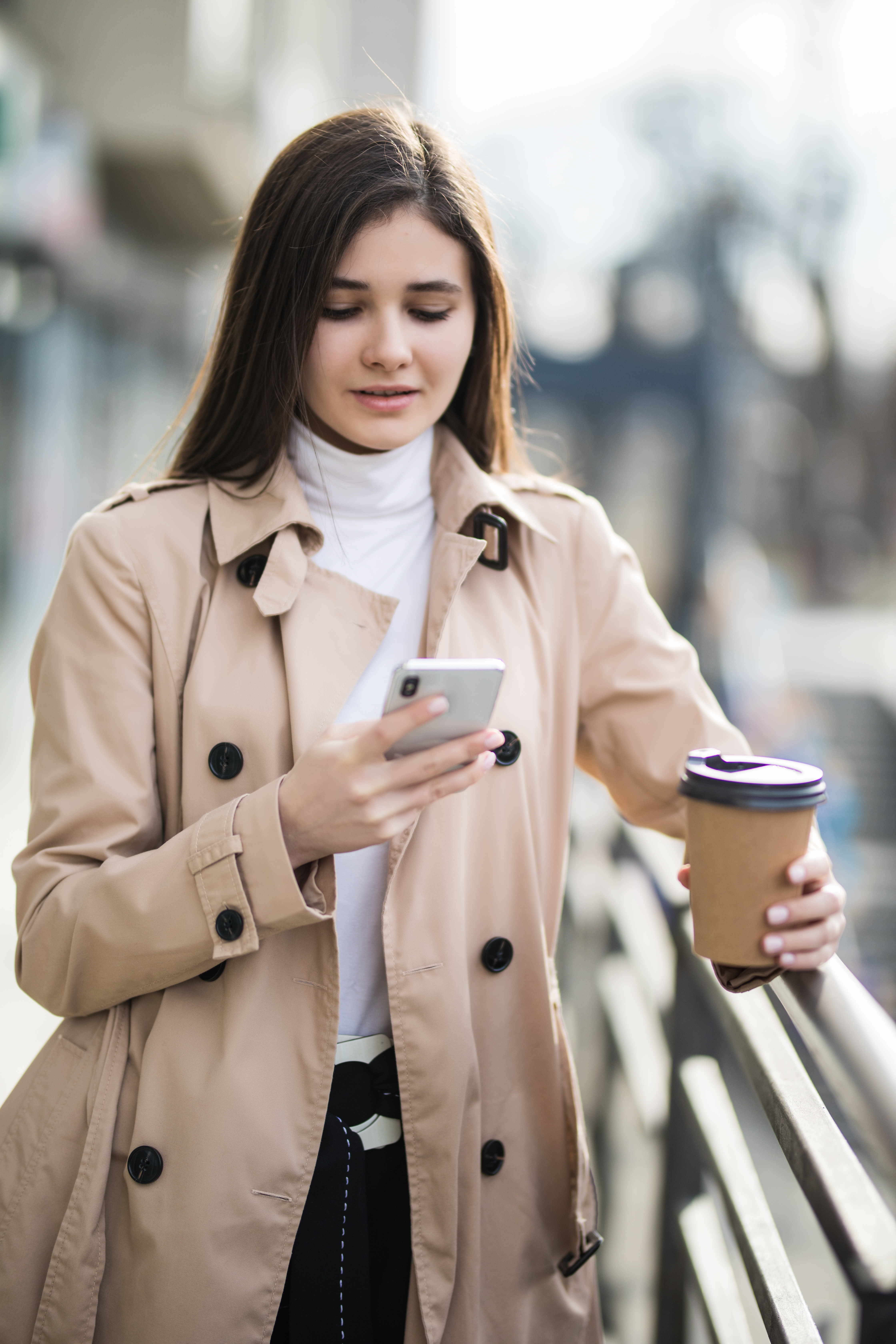 smiling-young-woman-light-brown-coat-read-news-phone-outside.jpg