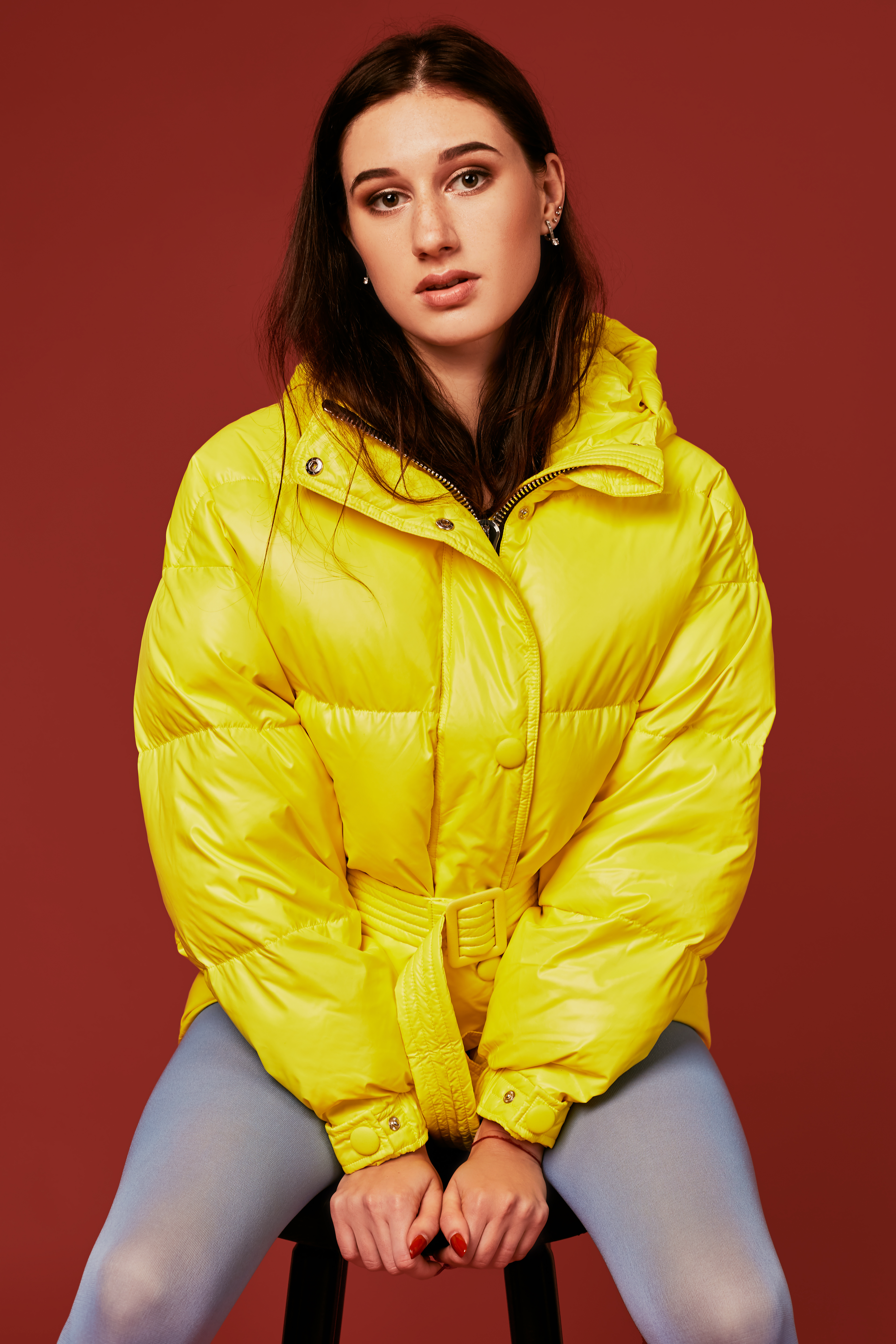 close-up-stylish-photo-cute-brunette-girl-wearing-yellow-oversized-down-jacket-posing-studio-red-background-using-chair.jpg